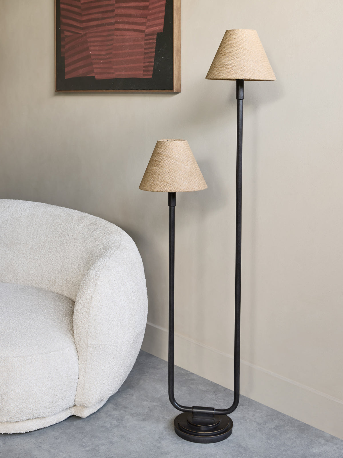 Staggered twin floor lamp beside a cream textured armchair against a neutral wall with framed red and black artwork.