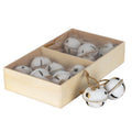 Angled view of cream-white bell ornaments in a divided pale-brown rectangular box, with two bells and their tan loops beside it.