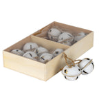 Angled view of cream-white bell ornaments in a divided pale-brown rectangular box, with two bells and their tan loops beside it.