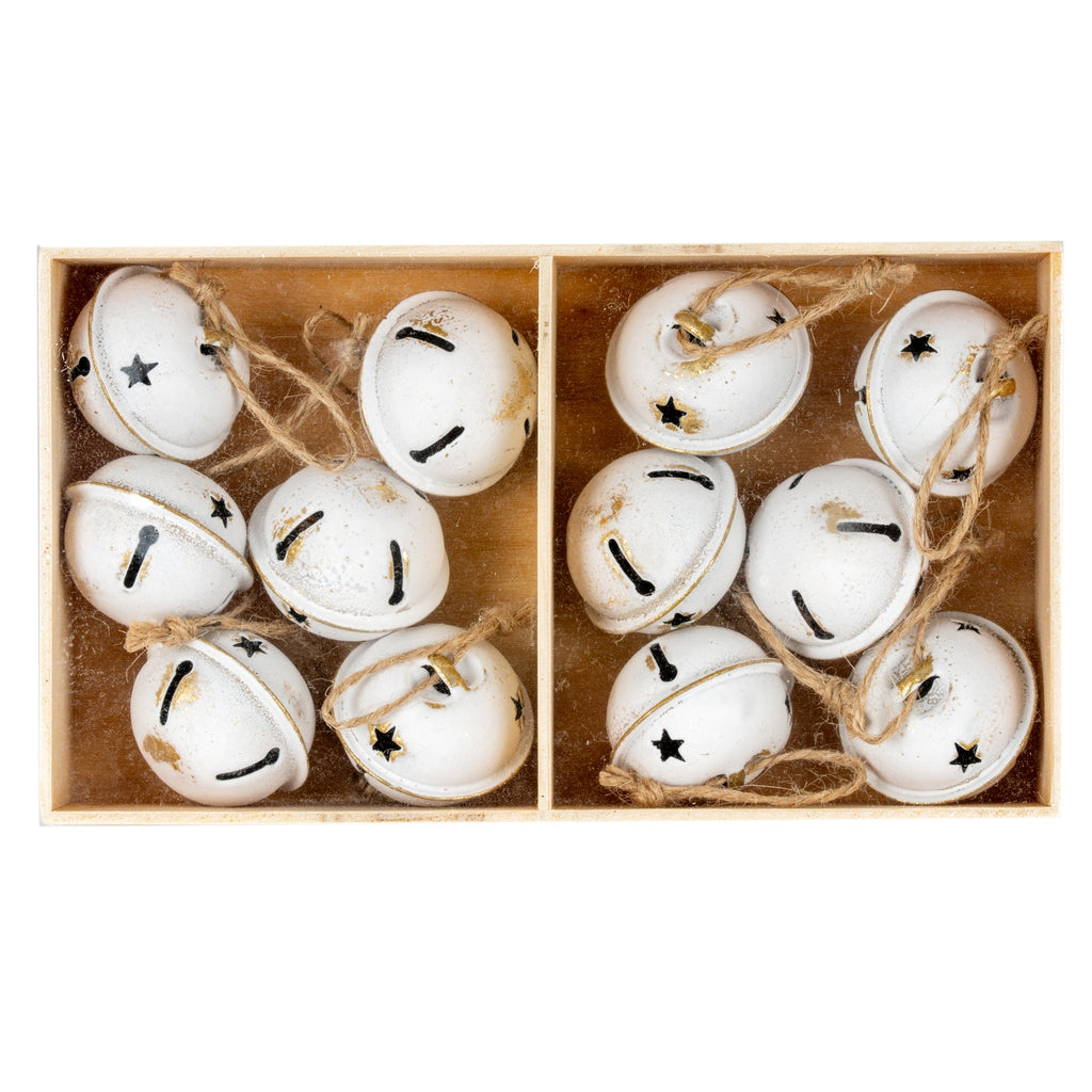 Overhead view of rounded cream-white bells arranged in two box compartments, showing star and keyhole-shaped cut-outs, rubbed gold-brown accents and tan loops.