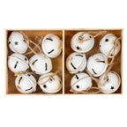 Overhead view of rounded cream-white bells arranged in two box compartments, showing star and keyhole-shaped cut-outs, rubbed gold-brown accents and tan loops.