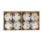 Overhead view of white rounded bells arranged in two box compartments, showing gold-brown patches, dark shaped openings and tan loops across the ornaments.