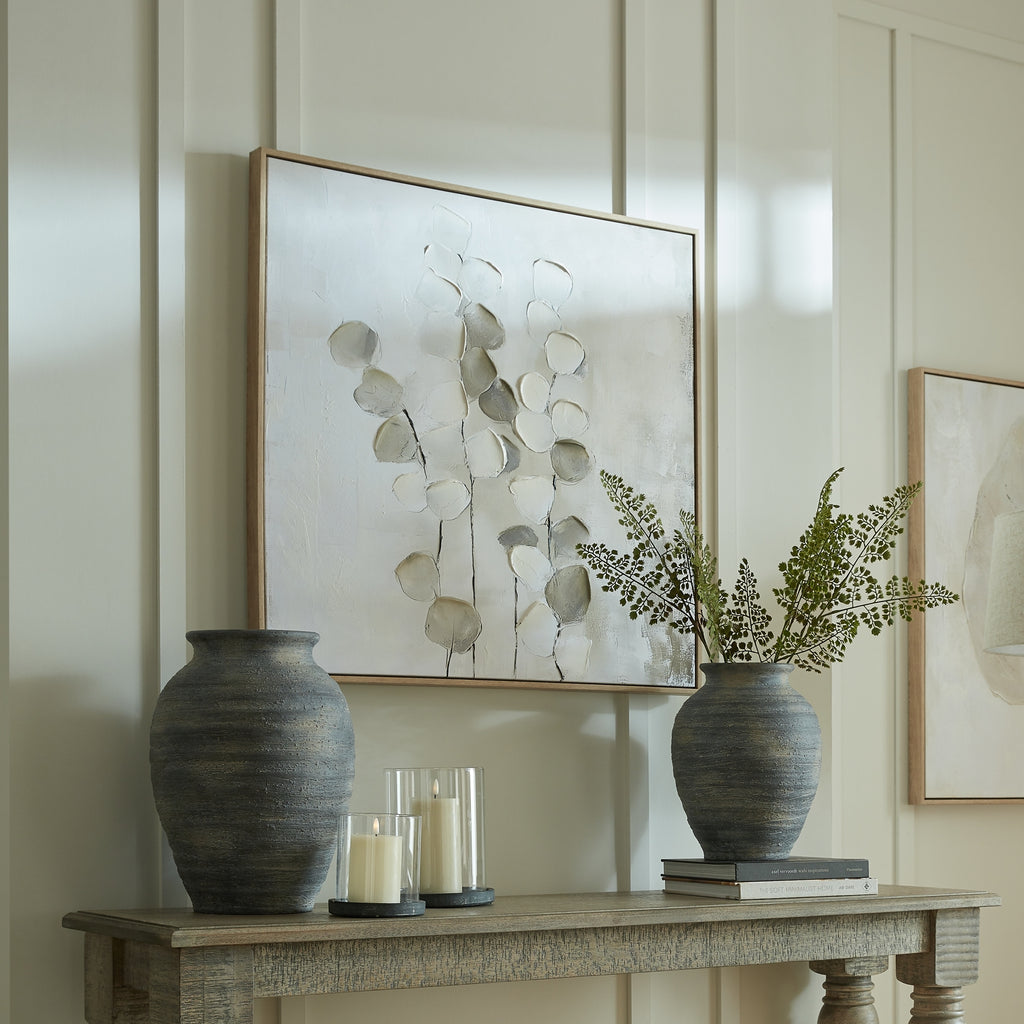 Stemmed Leafscatter artwork on a pale panelled wall above a console styled with dark vases, leafy stems, candles and stacked books.