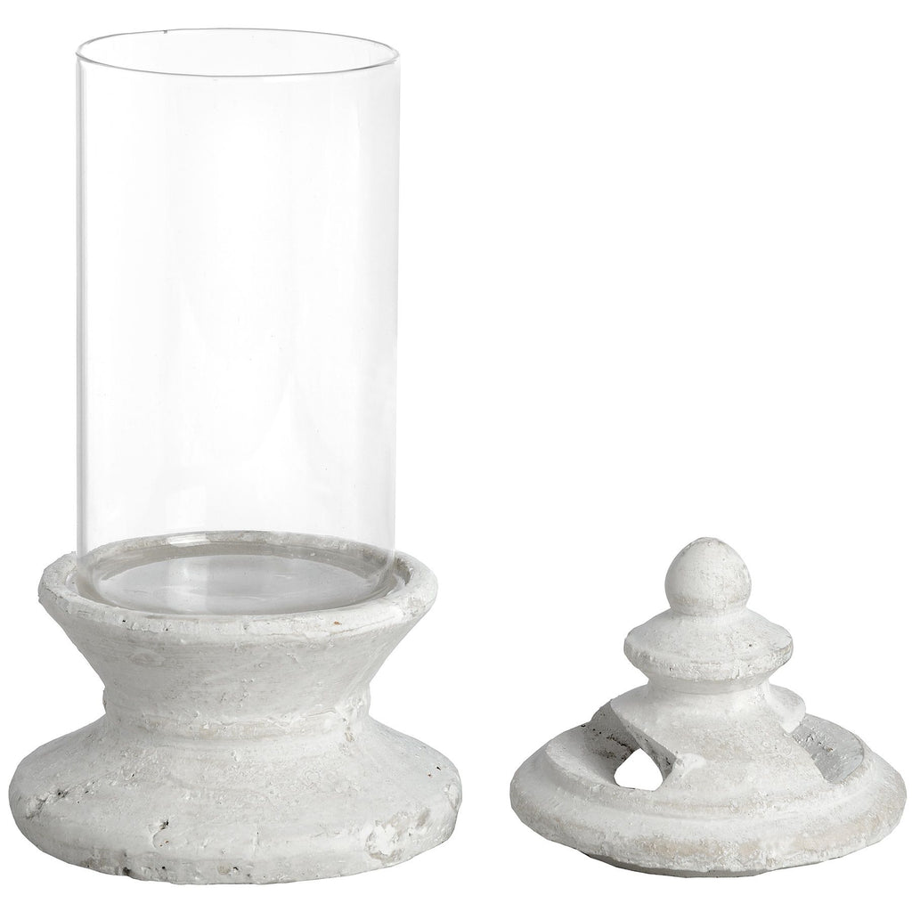 Candle holder with a clear cylindrical body on an off-white stepped pedestal, shown with the separate finial-topped lid beside it.