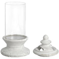 Candle holder with a clear cylindrical body on an off-white stepped pedestal, shown with the separate finial-topped lid beside it.