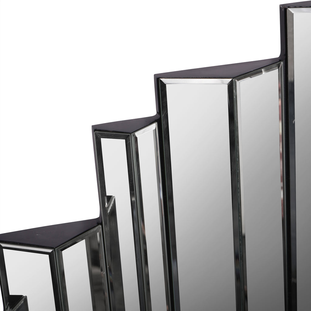 Detail of the mirror's stepped upper edge, showing adjacent bevelled panels and their angled faces.