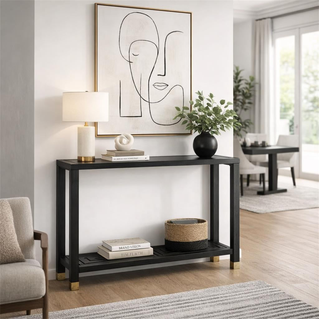Black console table beneath framed line art, styled with a lamp, books, a white sculpture and a leafy vase, with books and a woven basket on the lower shelf.