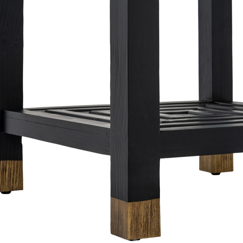 Close-up of a black table leg ending in a gold-toned section, with the patterned lower shelf behind it.