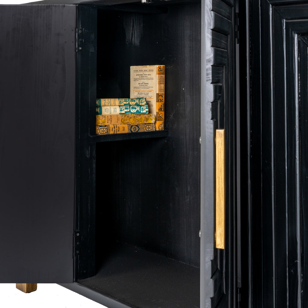 Sideboard detail with a door open, revealing a dark interior and a shelf styled with books beside the patterned front and brass-toned handle.