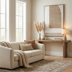 Brown arch artwork above a timber console with pale vases, dried grasses and a table lamp, beside a cream sofa with brown cushions.