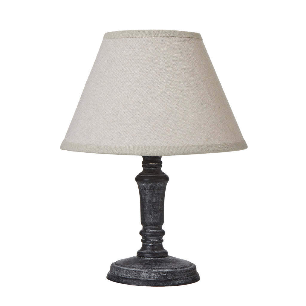 Table lamp with a wide tapered neutral shade, near-black shaped column and round foot against a white background.
