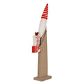 Angled full view of a tall brown elf decoration with a red striped pointed hat, white beard and patterned presents on a rectangular base.