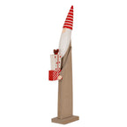 Angled full view of a tall brown elf decoration with a red striped pointed hat, white beard and patterned presents on a rectangular base.