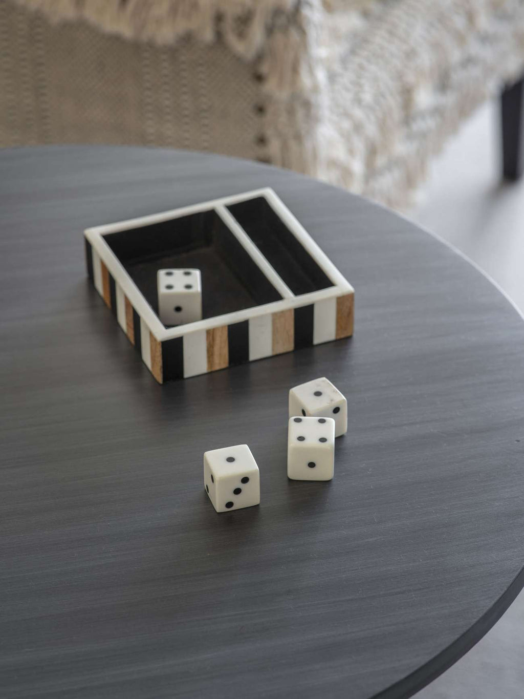 Striped tray on a round grey table with one white die inside and three dice set out in front.