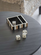 Striped tray on a round grey table with one white die inside and three dice set out in front.