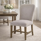 Pale grey stud-edged dining chair on a light rug beside a brown dining table set with stacked white plates and a vase of white flowers.