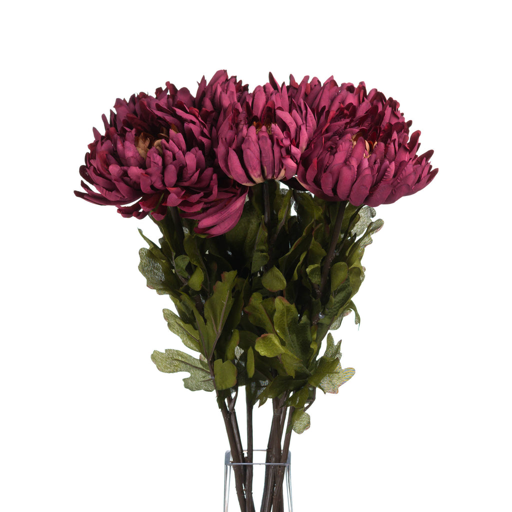Several burgundy-purple artificial flowers grouped in a clear vase, with layered petals and green leaves shown against white.