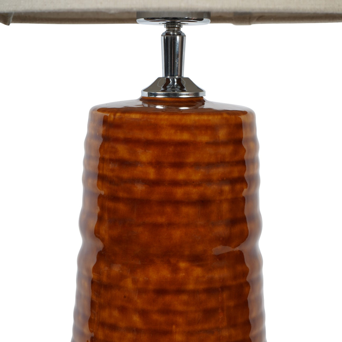 Close-up of the glossy amber-brown ceramic ribs and reflective neck beneath the linen shade.