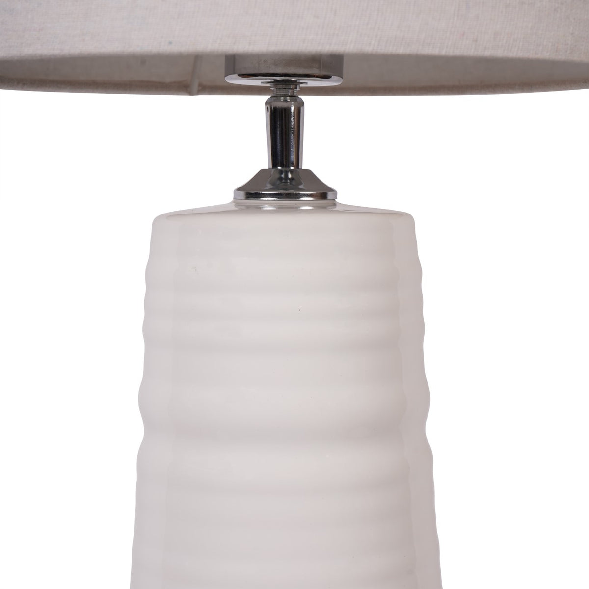 Close-up of the polished metal fitting between the white ribbed ceramic base and the fabric shade.
