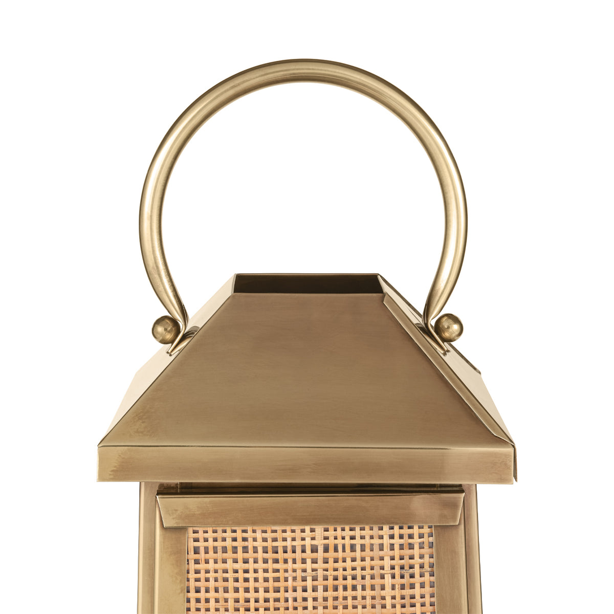 Close-up of the lantern's curved handle and sloping top in an antique brass finish, above the rattan panel.