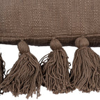 Detail of three full yarn tassels beneath the cushion seam and the uneven texture of the woven fabric.
