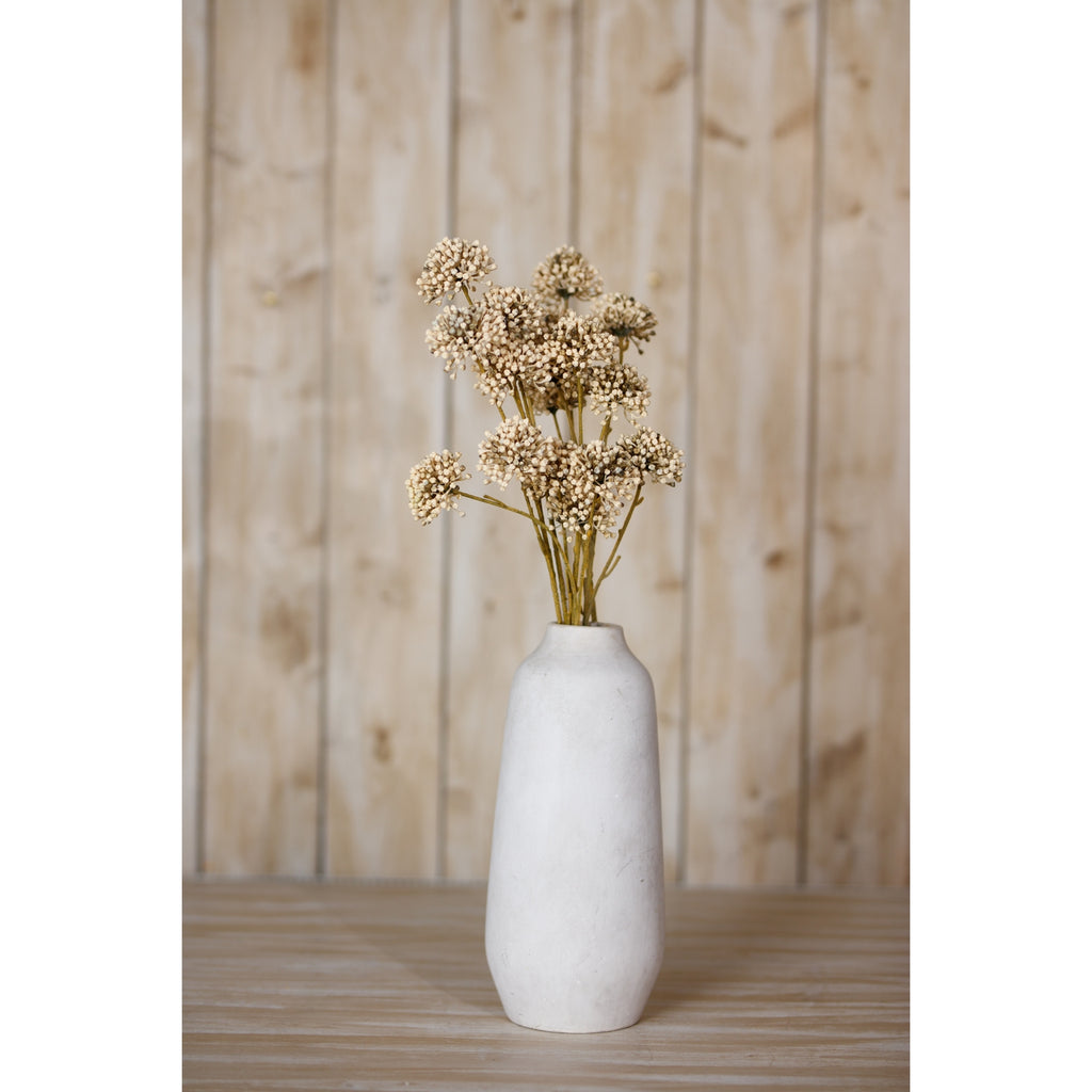Botanical sprays arranged in a tall off-white vase on a wooden surface in front of pale vertical wood panelling.
