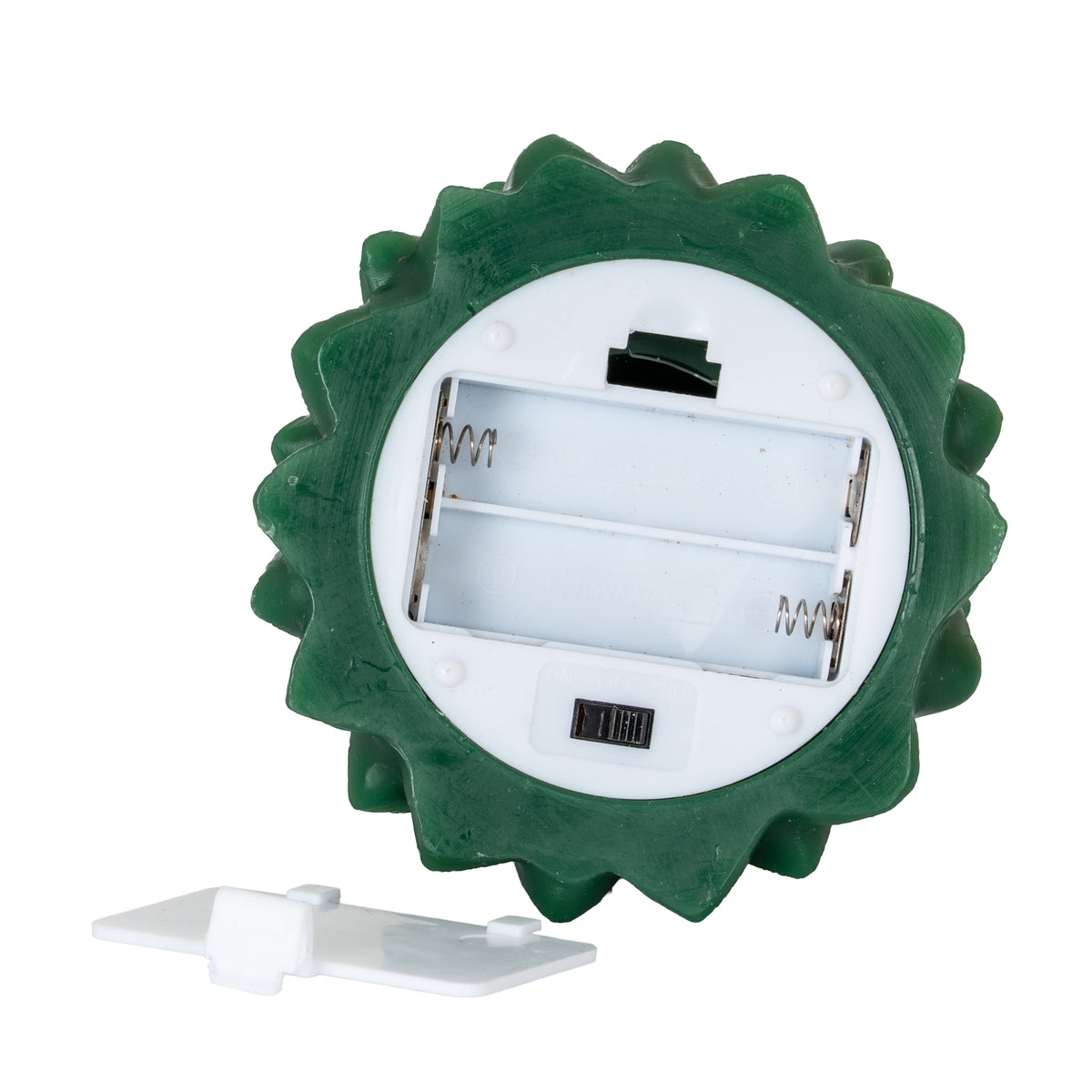 Underside of the green tree-form candle showing a white circular panel, an empty two-cell battery compartment, a black slide switch and the detached compartment cover.