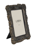 Angled view of a dark photo frame with a heavily textured irregular edge, warm metallic highlights, a cream insert and a rear tabletop support.