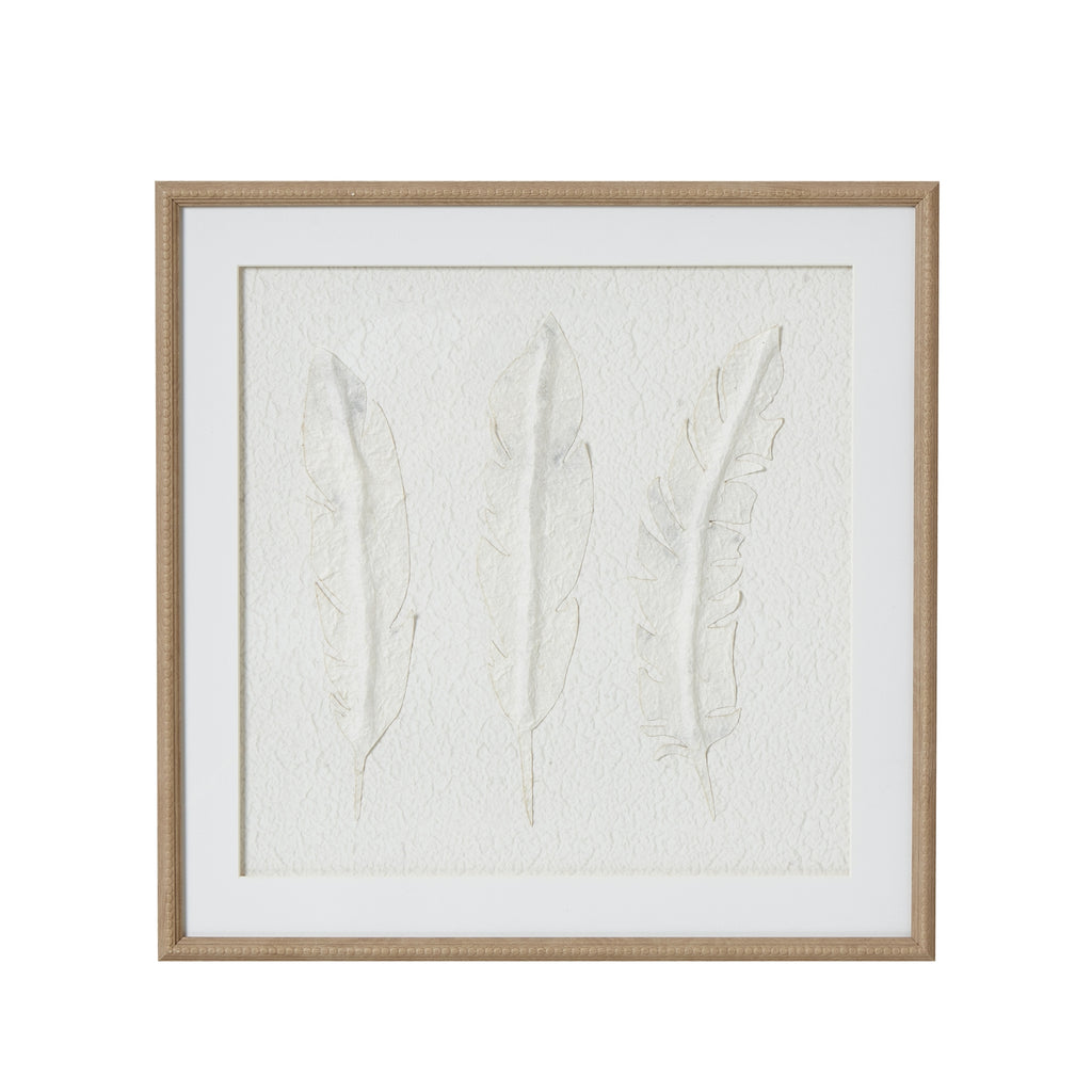 Front view of square framed artwork with three pale feather forms on a textured white background, a wide white mount and beige beaded frame.