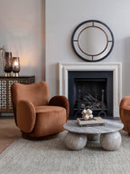 Living room with the round marble coffee table on a textured rug beside rust-coloured armchairs, beneath a fireplace mirror.