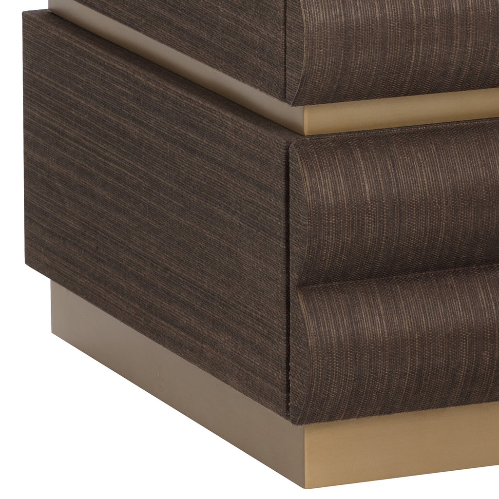 Detail of the nightstand's brown textured side, curved drawer edges and gold bands between the drawers and at the base.