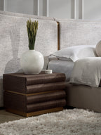 Tierfold Nightstand beside a pale upholstered bed, styled with a white vase of stems and a small candle.