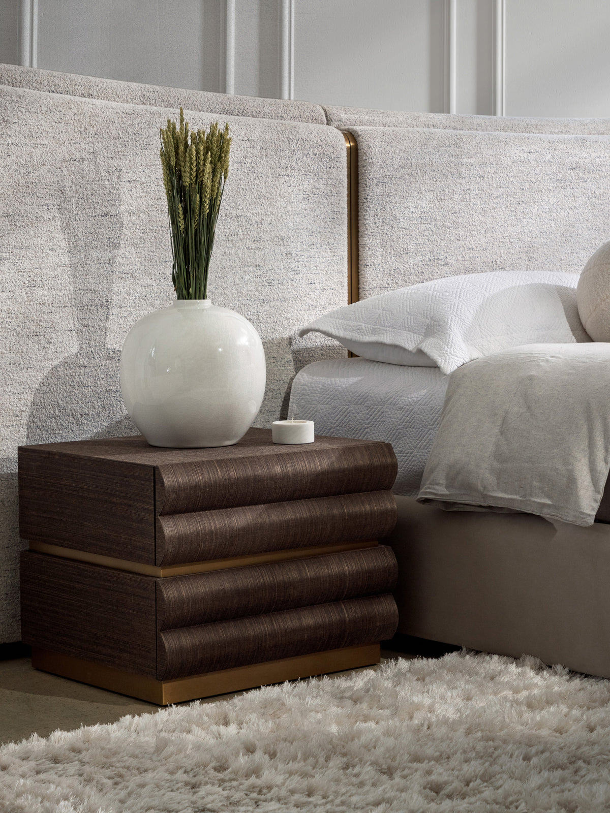 Tierfold Nightstand beside a pale upholstered bed, styled with a white vase of stems and a small candle.