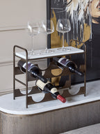 Wine rack holding three bottles with three wine glasses on its marble top, styled on a sideboard in front of abstract artwork.