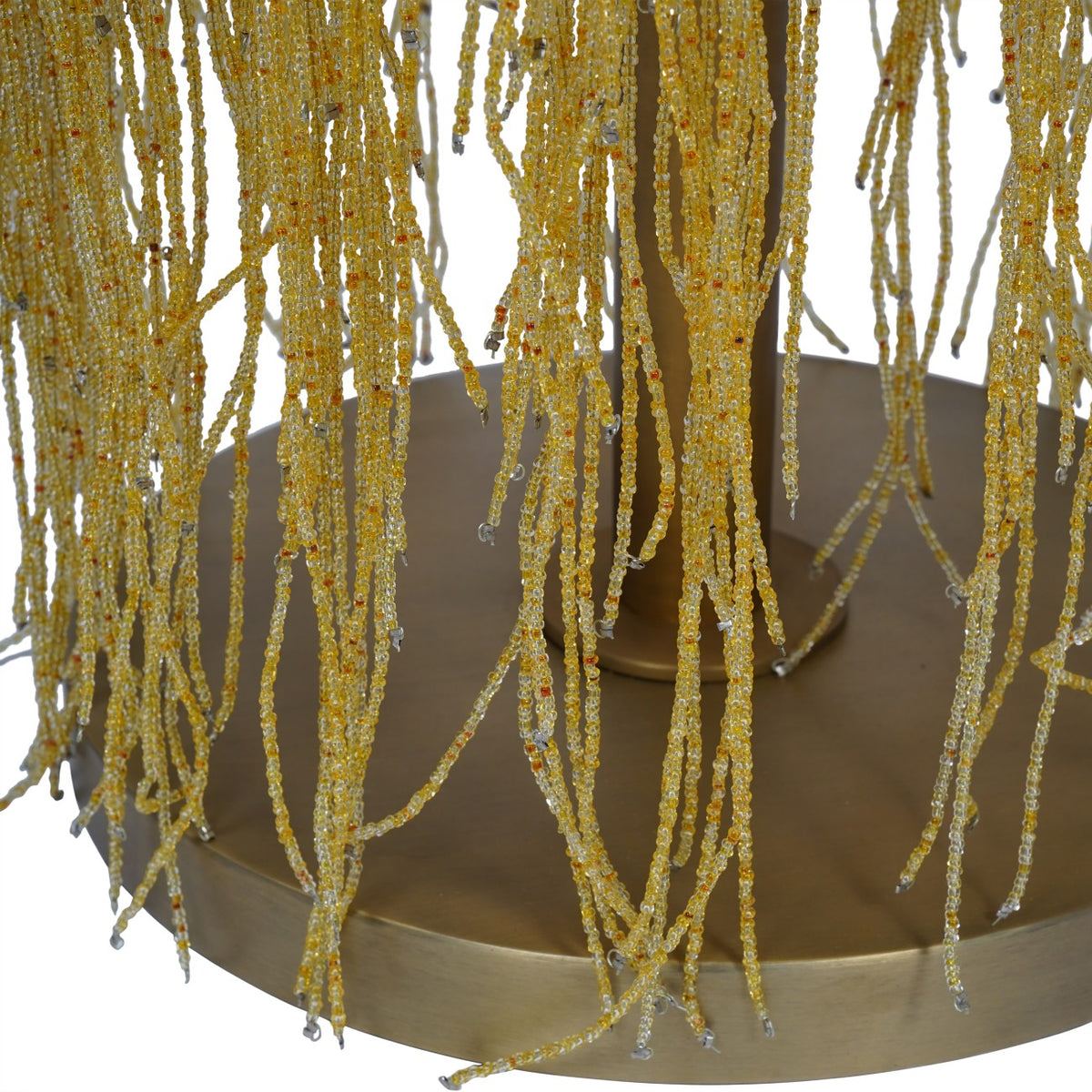 Close-up of loose amber glass bead strands hanging in front of the lamp's gold-toned round base and central stem.
