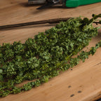 Close-up of the artificial amaranthus strands on a wooden surface, showing densely clustered green details with small rounded buds.