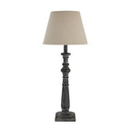 Unlit table lamp with a pale tapered shade, dark grey-washed turned column and stepped square base against white.
