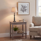 Table lamp pictured with its shade glowing on a side table beside books and a mug, beneath a framed branching print and next to a pale armchair.