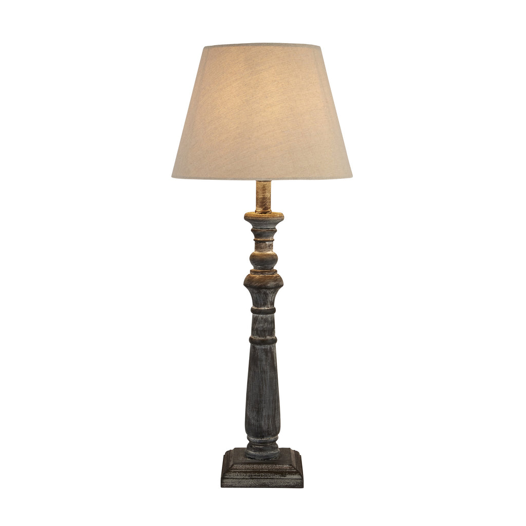 Table lamp pictured with a warm glow through its tapered shade, above a dark turned column and square stepped base on a white background.