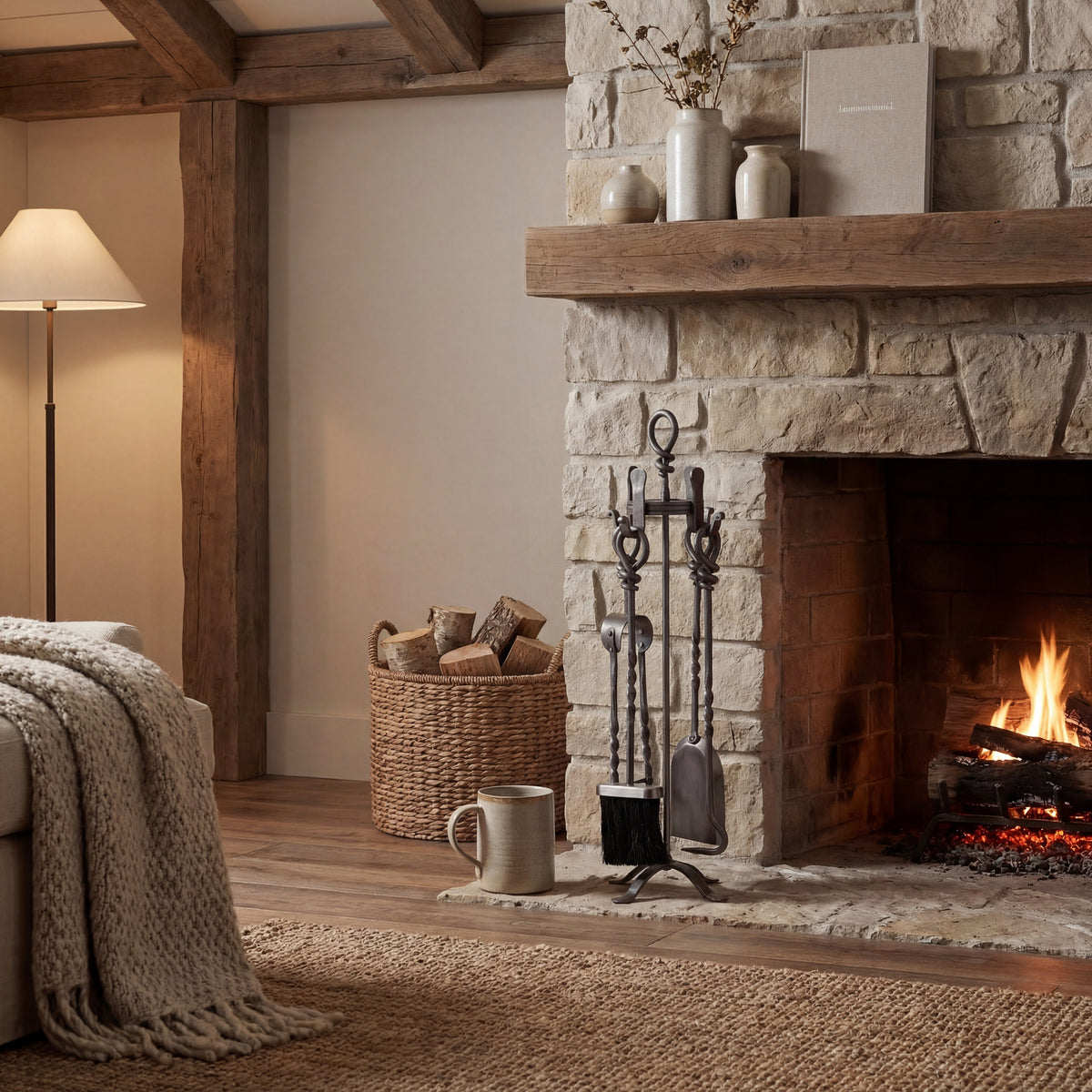 Twist & Knot fireplace tool set beside a lit stone fireplace, with a woven log basket, timber mantel and neutral furnishings.
