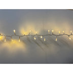 Close view of a twisted string-light cable stretched across a pale wall, with small illuminated points extending above and below the line.