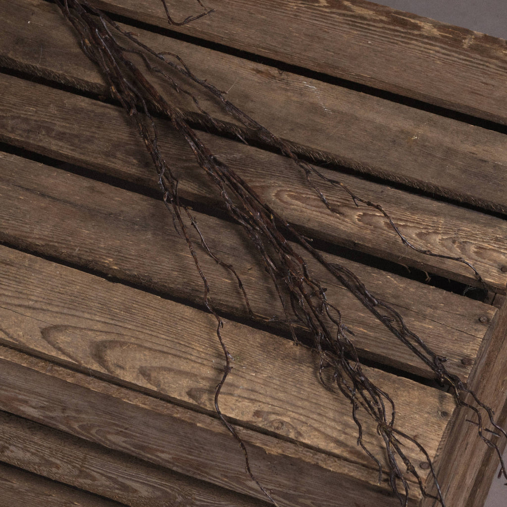 Close view of twisting dark-brown twiglets laid diagonally across wooden slats, showing ridged surfaces and small branching details.