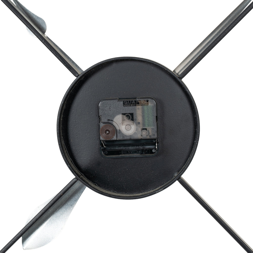 Rear close-up of the clock's black central disc, with a movement marked QUARTZ and an empty battery compartment between diagonal braces.