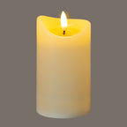 Cream LED candle photographed with a bright white flame-shaped element and yellow illumination around the recessed top, against a grey background.