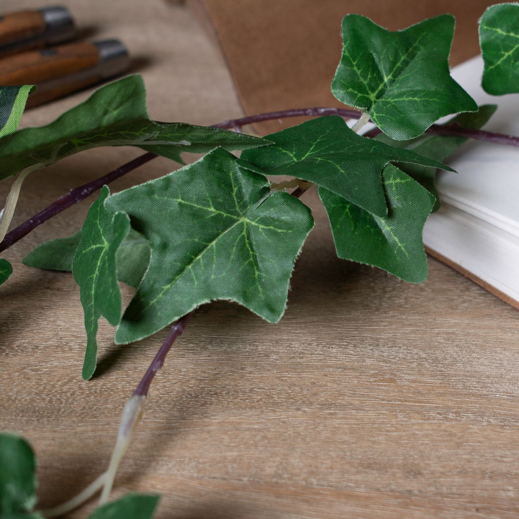 Detail of artificial ivy leaves and purple-brown vines resting on a wood surface beside an open book.