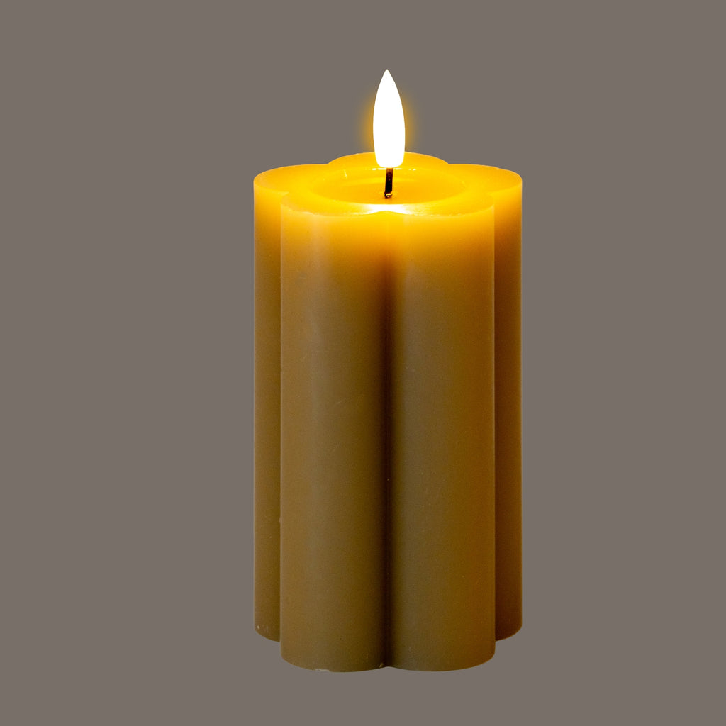 Lobed pillar LED candle shown illuminated against a grey background, with a bright white flame-shaped element and a golden glow around the recessed top.