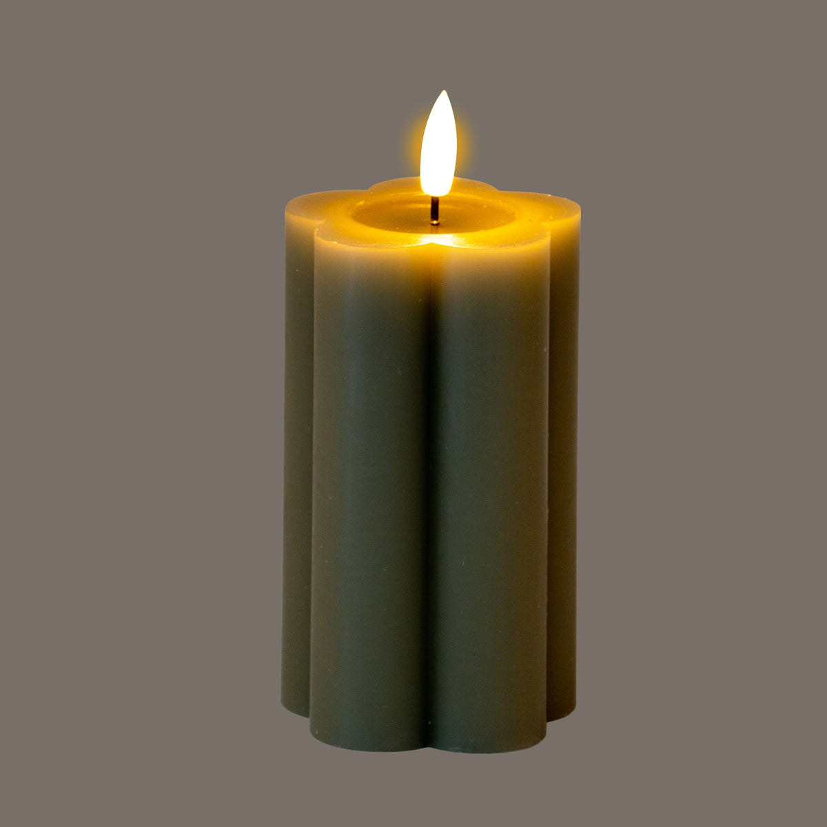Grey-green lobed pillar LED candle photographed with its flame-shaped element illuminated and yellow light around the recessed top against a grey background.