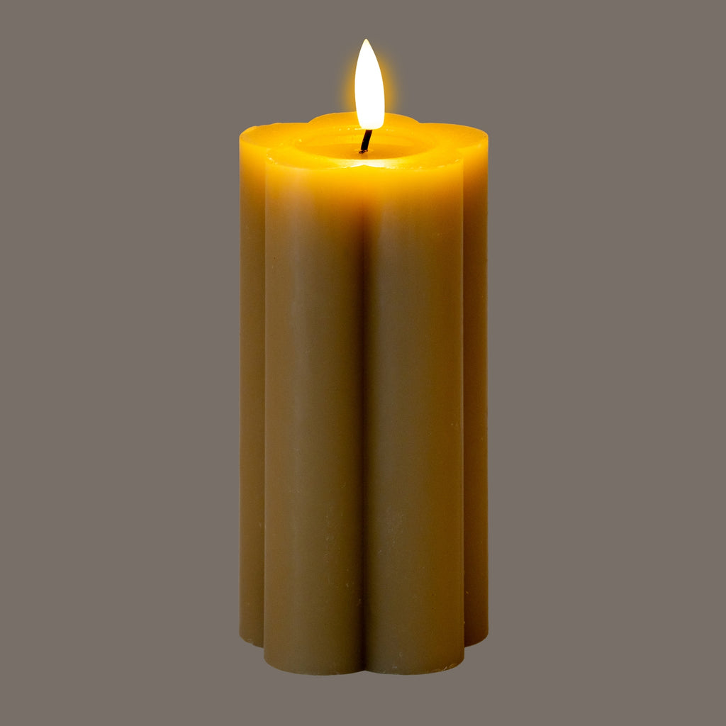 Lobed pillar candle photographed against a grey background, with a bright flame-shaped tip and a yellow glow across the recessed top.