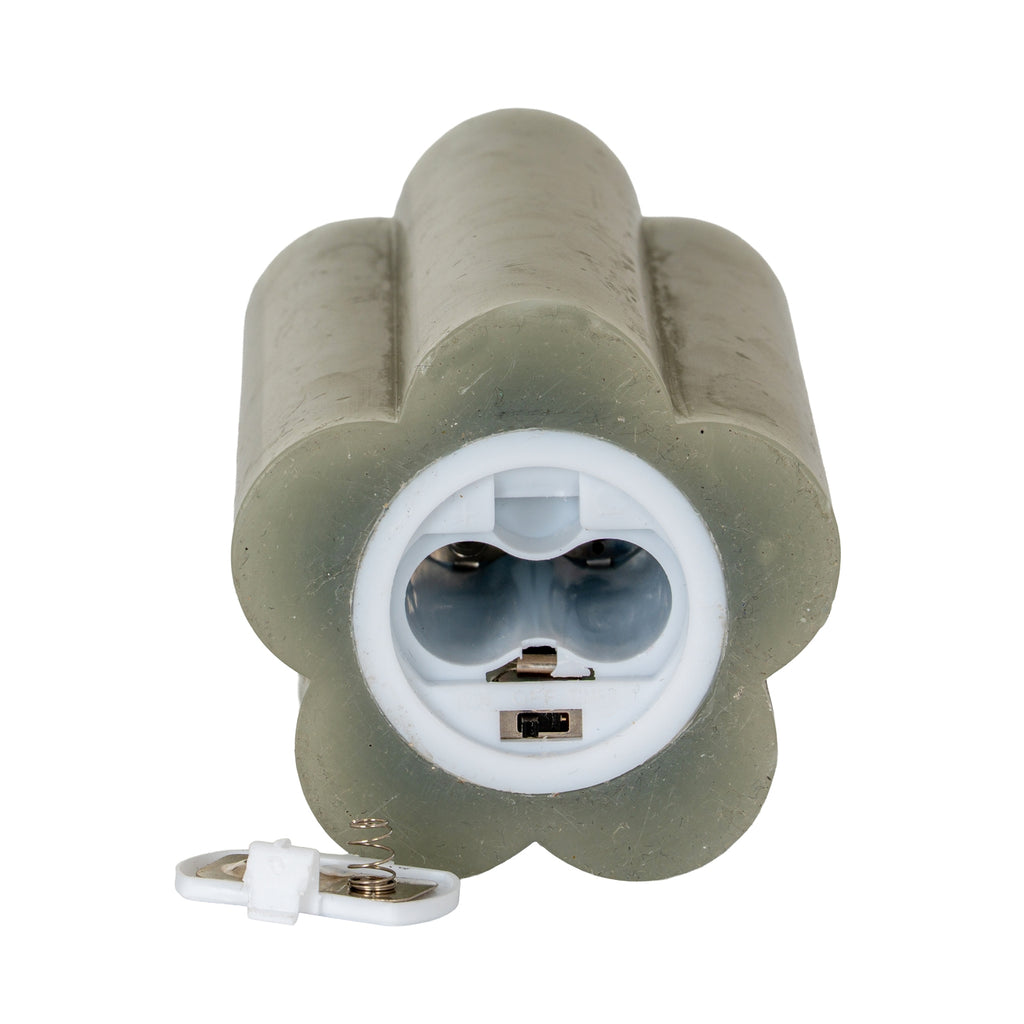 Underside of the lobed candle showing two empty battery bays in a white circular housing, a small slide switch and the detached cover with a spring contact.