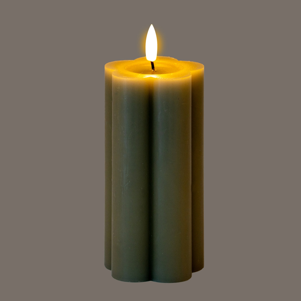 Lobed grey-green pillar LED candle photographed illuminated, with a bright flame-shaped tip and golden light around the recessed top.